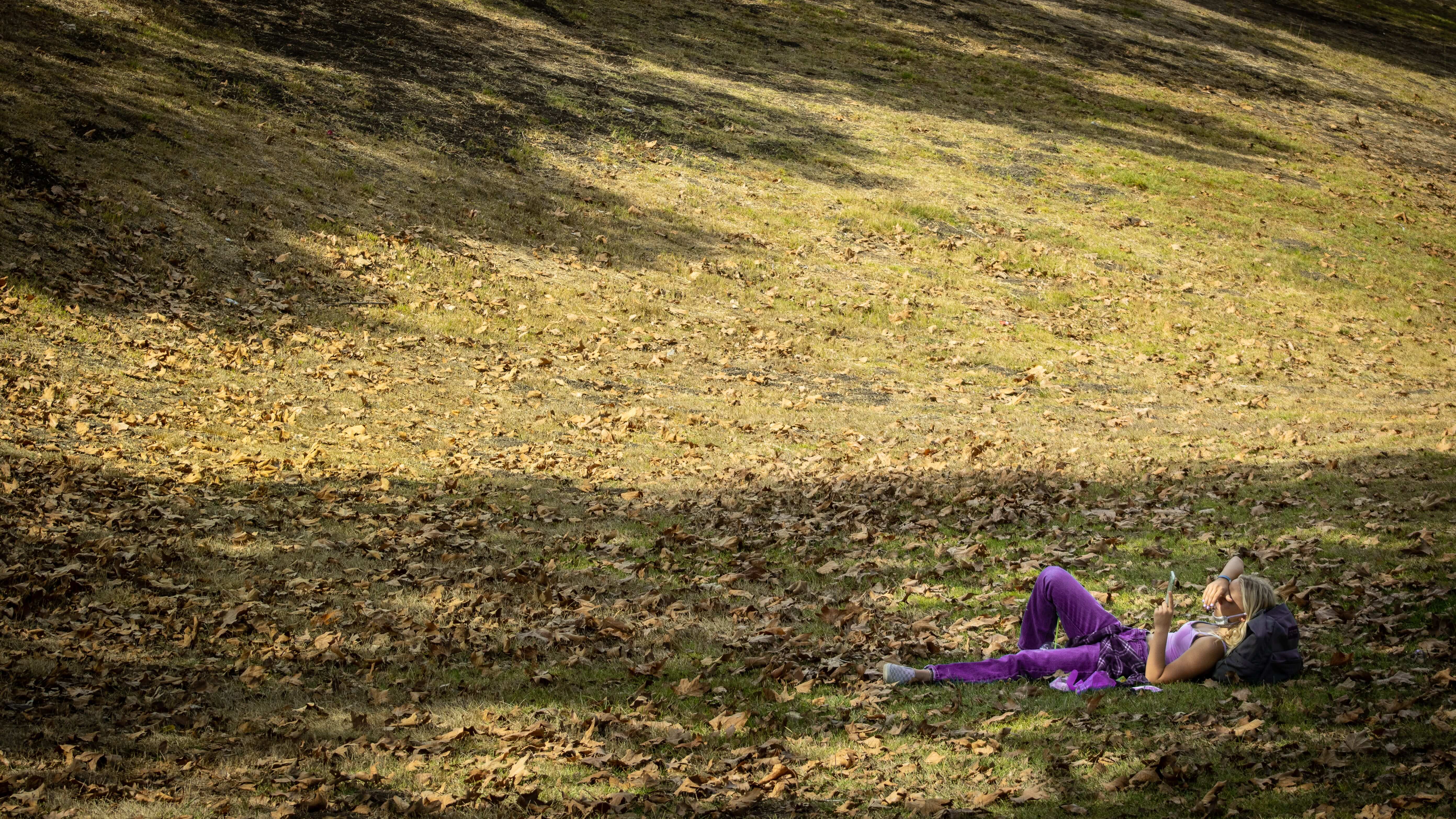 A photograph of a young woman wearing purple laying in a field of grass